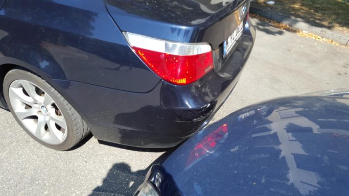 Zwei parkende Autos, eines in dunklem Blau und das andere im Vordergrund, sichtbar beschädigt.
